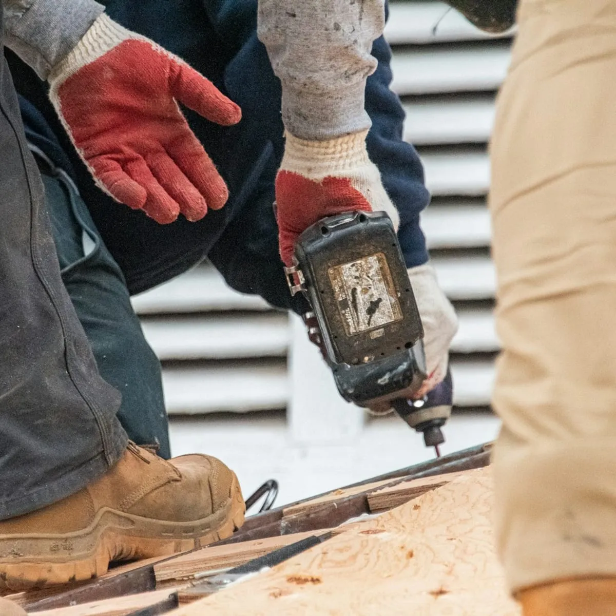 Gloved hands driving a cordless drill into timber on a job site