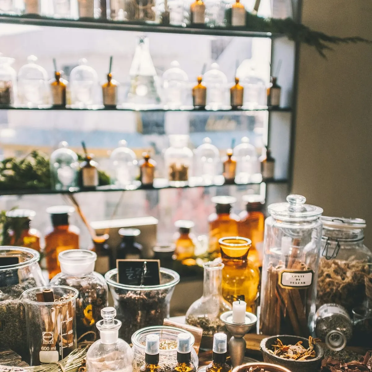 Amber bottles and open jars of dried herbs on an apothecary table