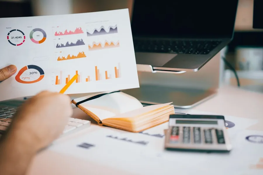 A hand marking up printed charts beside a notebook and calculator