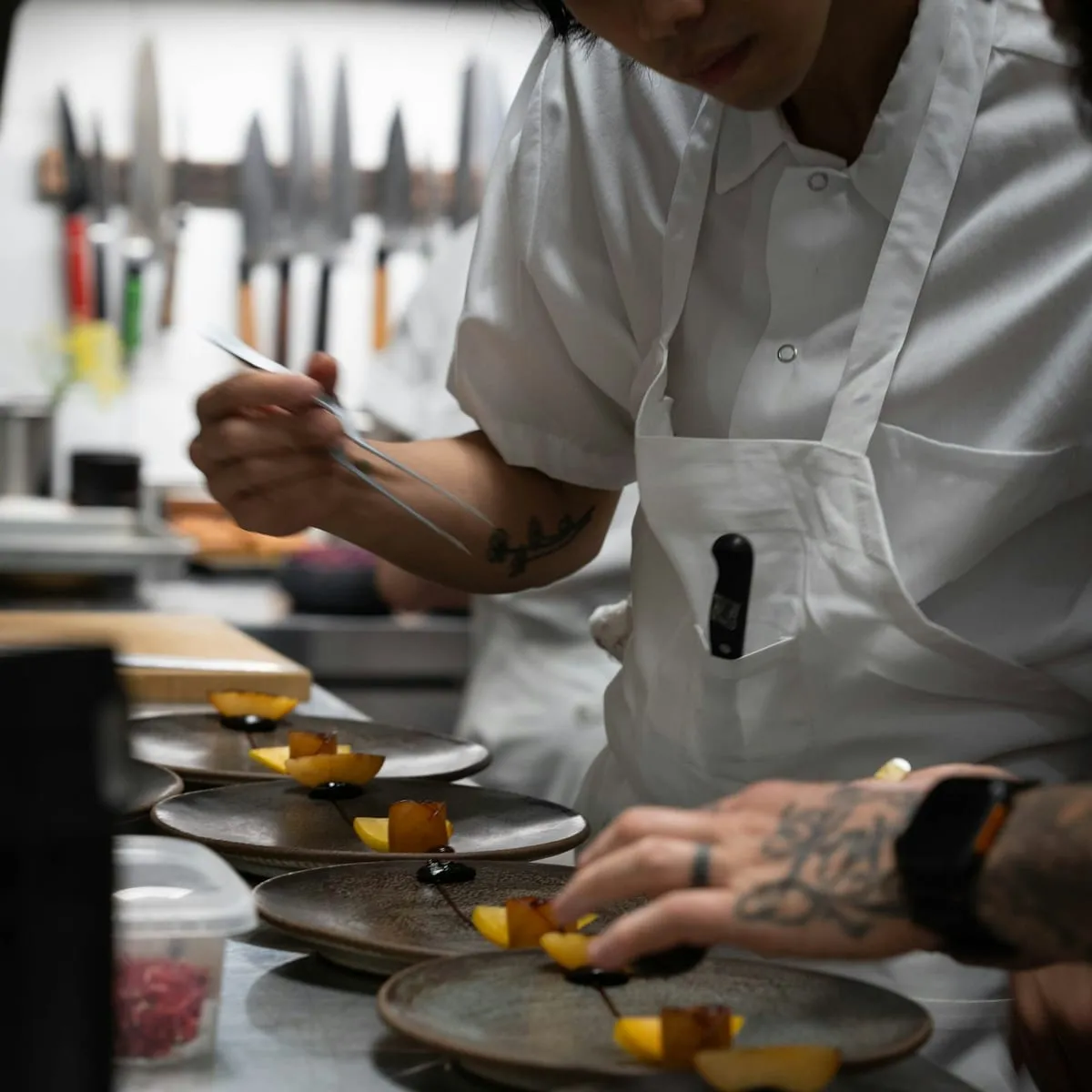 A chef plating a row of dishes along a stainless steel pass in a restaurant kitchen