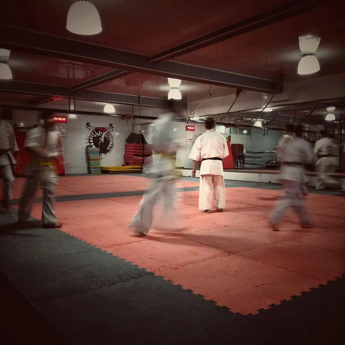 Students in white gi moving through a drill on the red mats of a dojo