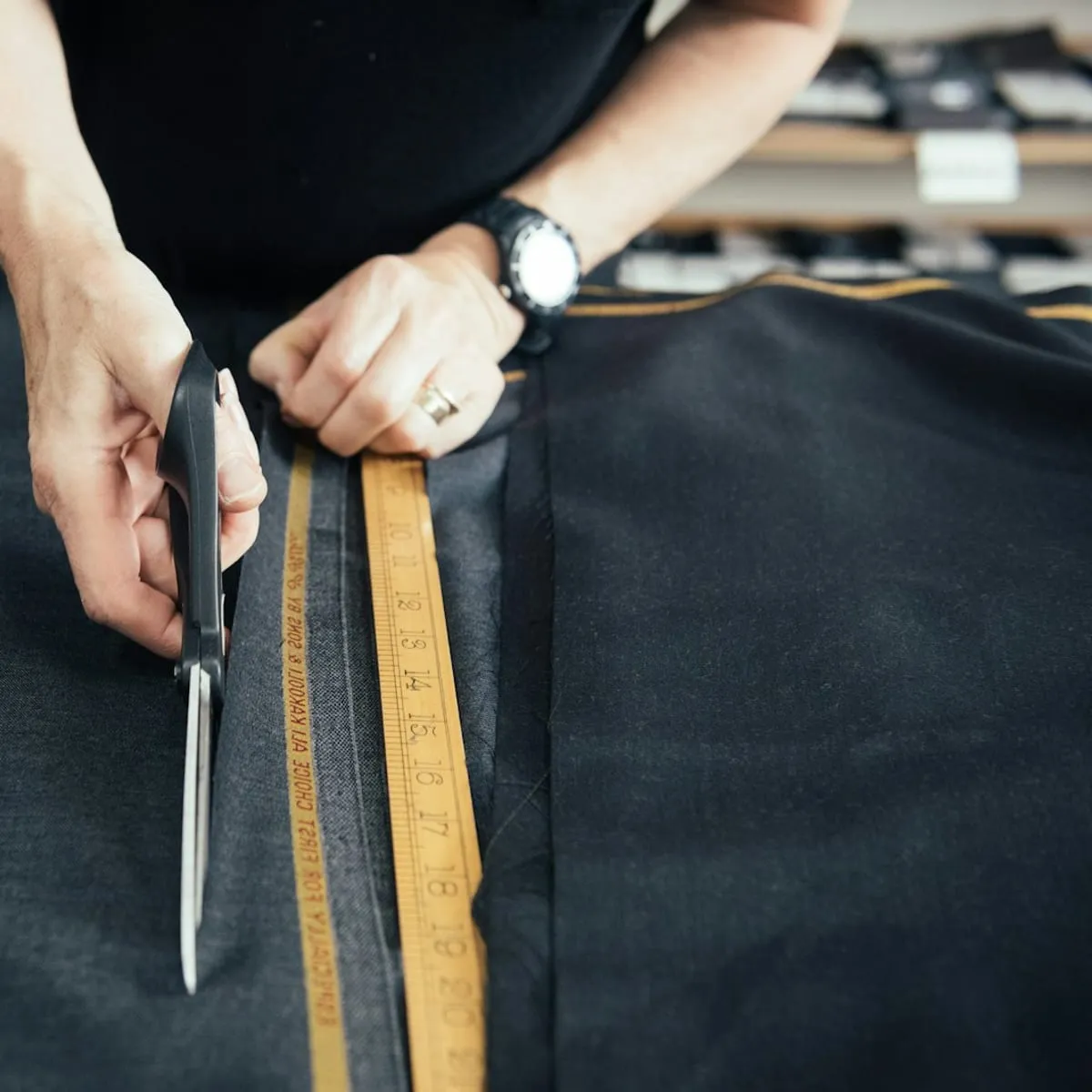 A tailor cutting dark fabric with shears beside a tape measure