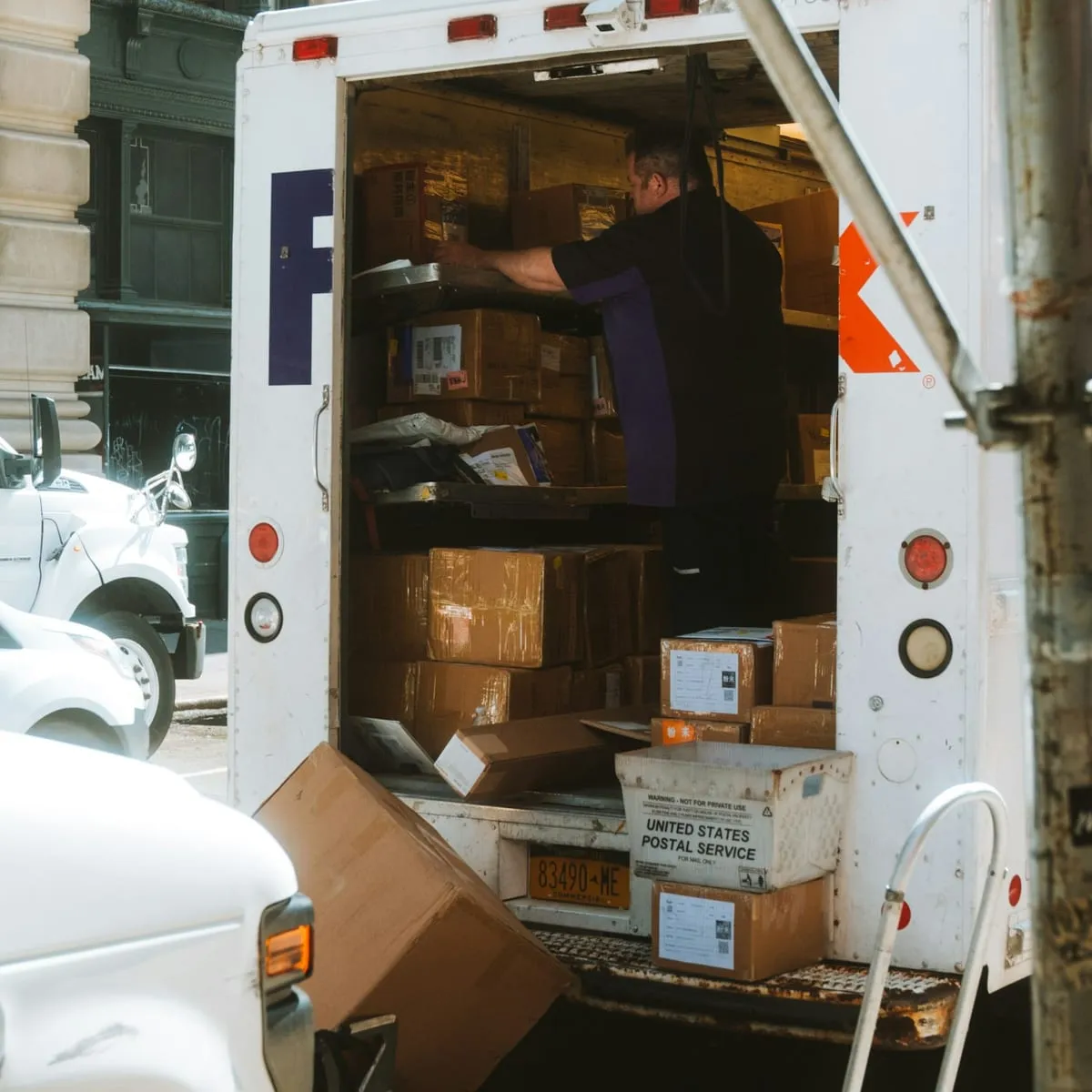 A driver loading parcels into the open back of a box truck at the curb