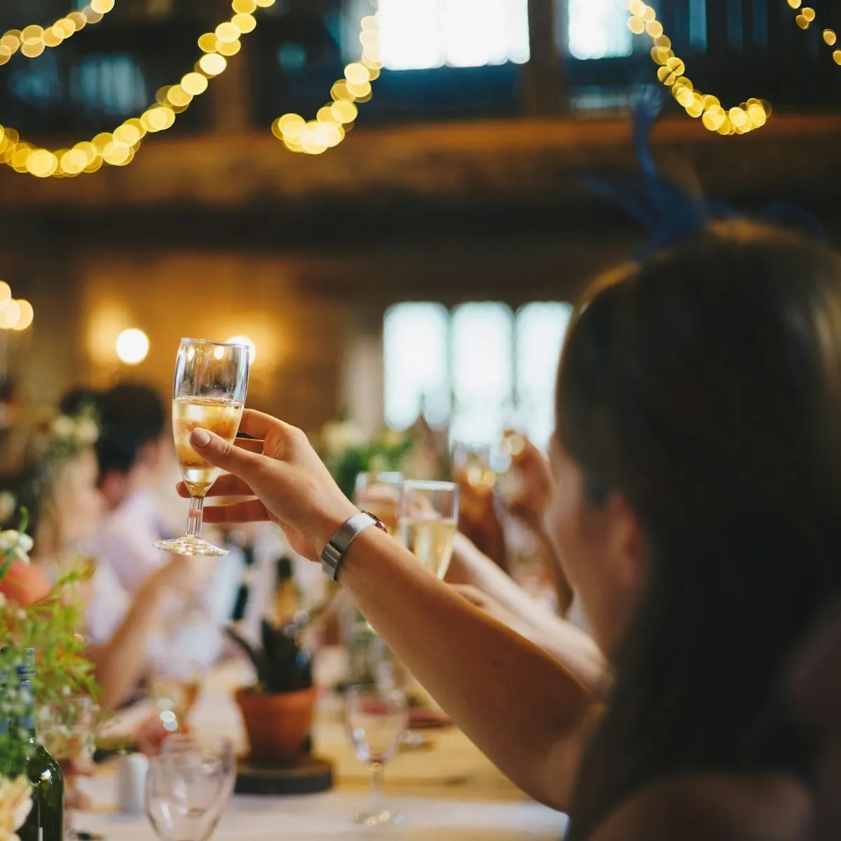 Guests raising glasses at a long table under strings of lights