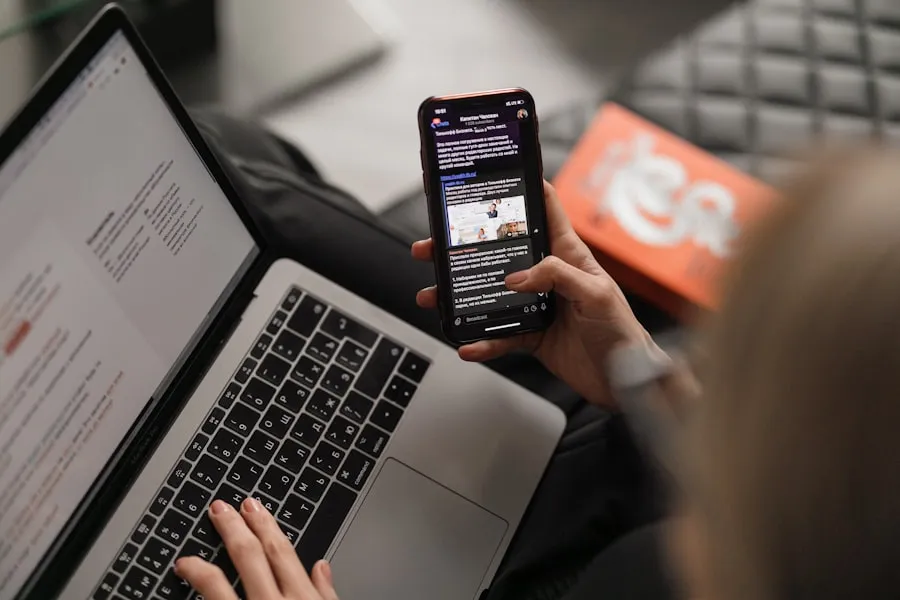 Someone holding a phone showing a web page while working at a laptop